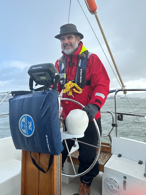 A photo of me at the helm of a sailboat in the San Francisco Bay.